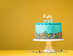 Blue buttercream birthday cake with colorful sprinkles over yellow background.