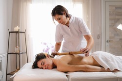 Beautician masseur doing relaxing massage with bamboo stick cane on woman back.