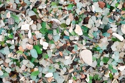 The texture of a stone beach with many pieces of colored glass turned by water.