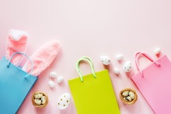 Easter shopping background with green and pink shopping bags with Easter bunny ears and Easter eggs and bird's nest on pink background
