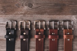 Leather belts in different colors for jeans and chinos on the wooden surface.