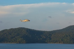 Grey Helicopter flying over the mountain and sea with blue sky.