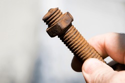 old rusty bolt, iron rod with screw threads, in hand. Rusted mechanical components. holding threaded bolt and nut. dismantling concept, difficult to unscrew, non-removable. isolated on light, close-up