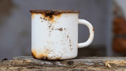 metal old dirty cup isolated. rusty iron cup, close-up. old tea utensils. a white mug stands on a wooden board