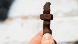 old rusty bolt, iron rod with screw threads, in hand. Rusted mechanical components. holding threaded bolt and nut. dismantling concept, difficult to unscrew, non-removable. isolated on light, close-up