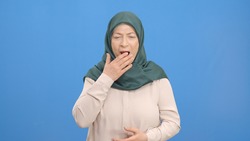 Sleepy, yawning old woman in a turban. Portrait of a sleepy old woman.Indoor studio shot isolated on blue background.