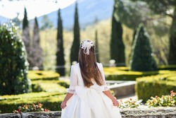 Girl in white communion dress with bow on her back in a park for a photograph