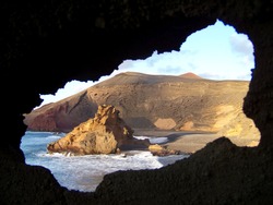 Amazing view at the black beach and the rock in the ocean from the hole with blurry edge in the mountain in Lanzarote, Canary islands. The outline of the hole reminds the shape of the island