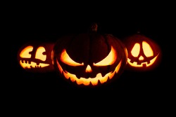 Three Halloween pumpkins with glowing eyes and mouth on a black background	