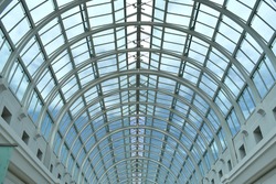 close up of arched glass domed steel structured window roof creating semi circle patterns letting daylight into building, looking through glass to blue sky and clouds
