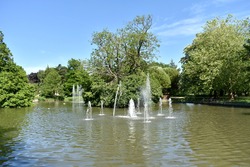 landscape image of lake with water fountain feature spurting water in front of trees with a clear deep blue sky in summer time