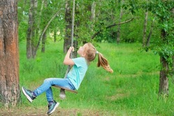 Child having  fun outdoors swinging on wooden homemade swing tied to a tree with a rope in spring or autumn.