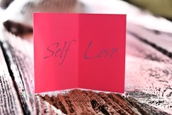 Sefl Love word, text. Soft focus of pink note card on pink wooden background, close-up. Cozy, soft , minimal. Love and take care yourself concept