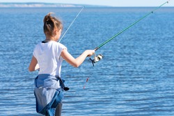 A young teenage girl stands on the Bank of the river and holds a spinning rod in both hands, fishing. Morning fishing. A girl fishing with a fishing rod near the river.