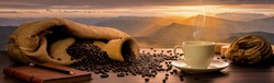 Concept Banner,Many coffee beans are laid on wooden barrels and all around, and there are coffee cups with notebooks and pencils on wooden tables, with a backdrop of high mountain views in the morning