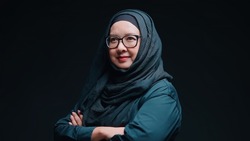 An office worker for an Asian Muslim woman stands with arms crossed with a happy face and a commitment to work, on black background.
