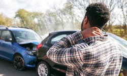 Young man rubbing neck in pain from whiplash injury standing by damaged car after traffic accident