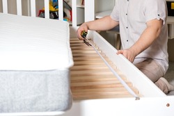 A man assembles a children's bed, measures the length with a tape measure, hands close-up.