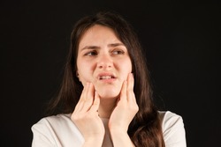 A woman holds her hands to a sore temporomandibular joint, dysfunction and pain, dislocated jaw, problems of wisdom teeth.