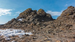 Granite rocks, devoid of vegetation, against the background of the blue sky. Cracks and yellow lichens on the rocks. Snow and dry grass on the ground. Siberia. Sunny winter day