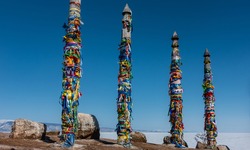 High wooden ritual pillars are tied with colorful ribbons. Bright colors against the background of a clear blue sky and white ice of a frozen lake. Picturesque boulders on the ground. Baikal 