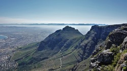  View from the top of Table Mountain in Cape Town. There are winding roads on the slopes. There is a city in the valley. On the horizon, a mountain range is visible in the haze. South Africa          