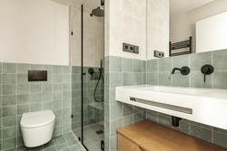 Bathroom of a house with contemporary decoration of small green tiles, black details in faucets and accessories, frameless mirror and white resin sink