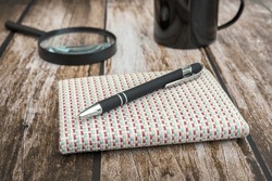 A small note pad with woven covers and a black pen on top