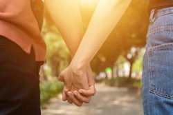 Couple hold hands in the autumn or summer park on sunset. Closeup of loving couple holding hands while walking. Selective focus