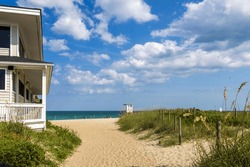 A gorgeous summer landscape at the beach with blue ocean water, silky brown sand, lush green plants and grass, a lifeguard tower, blue sky and clouds in Wrightsville Beach North Carolina USA