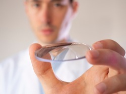 Oculist holds a lens in his hand. Eyewear lens.