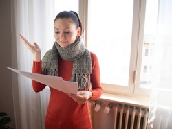 Heating bill. Increase in the cost of gas bill. Soaring energy prices. Increase in the price of natural gas. Energy crisis in Europe. Person holds heating bills in hand near the radiator. 