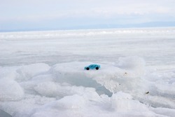 A blue toy car stands on a block of white ice against a background of white ice and a bright sky