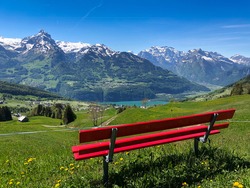 Red bench in the foreground with a view of the lake and mountains in Switzerland, blue sky