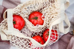 Big delicious red tomatoes are lying in a grid.Fresh healthy food.Eco friendly bag with shopping products.Ripe juicy vegetables.Harvest in the summer and autumn in the garden.Zero waste