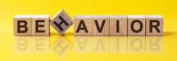 BEHAVIOR Word made of building blocks on a light yellow background, the reflection in the surface