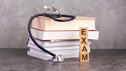 the word exam is written on wooden cubes near a stethoscope on a paper background. concept of medical education with book and stethoscope.
