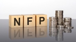 NFP. wooden cubes. blocks lie on a black background. stacks with coins. inscription on the cubes is reflected from the surface of the table. selective focus. NFP - short for Non-Farm Payroll