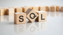 SQL - Structured Query Language - an abbreviation of wooden blocks with letters on a gray background. Reflection of the caption on the mirrored surface of the table.