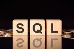 sql - short for structured query language. text on wood cubes with coins, black background, business concept. the inscription on the cubes is reflected from the surface of the black table. front view