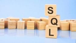 on a bright blue background, wooden blocks and cubes with the text sql. cubes is reflected from the surface. sql - short for structured query language