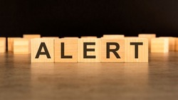 word Alert is written on wooden cubes standing on black background