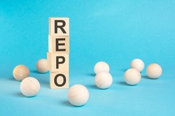 a pyramid of wooden cubes with the word REPO and wooden balls around on a bright blue background, copy space on the right. REPO - short for Repurchase Agreement