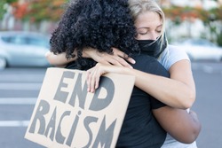 Young african woman hugging a white northern woman after a protest - Northern woman with end racism bannner in her hands - Concept of no racism 