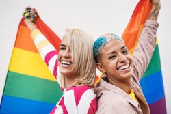 Cheerful young couple of women with rainbow flag at gay pride event - Focus on face