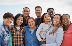 Group of multigenerational people hugging each other while smiling on camera - Multiracial friends having fun together outdoor