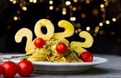 Figures, numbers  2020  made from cheese on a spaghetti slide with pesto sauce and cherry tomatoes on black