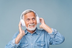 Studio portrait of relaxed cheerful man wearing and holding wireless headphones isolated on blue wall, enjoying listening to favourite music soundtrack, wellbeing, meditation concept