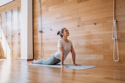 Full length view of the senior fit woman making cobra pose on yoga mat, exercising at home at the light room. Sport and recreation concept