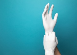 White latex gloves on two hands with a vibrant blue studio background. One gloved hand is pulling the end of the other glove down to simulate putting gloves on. 